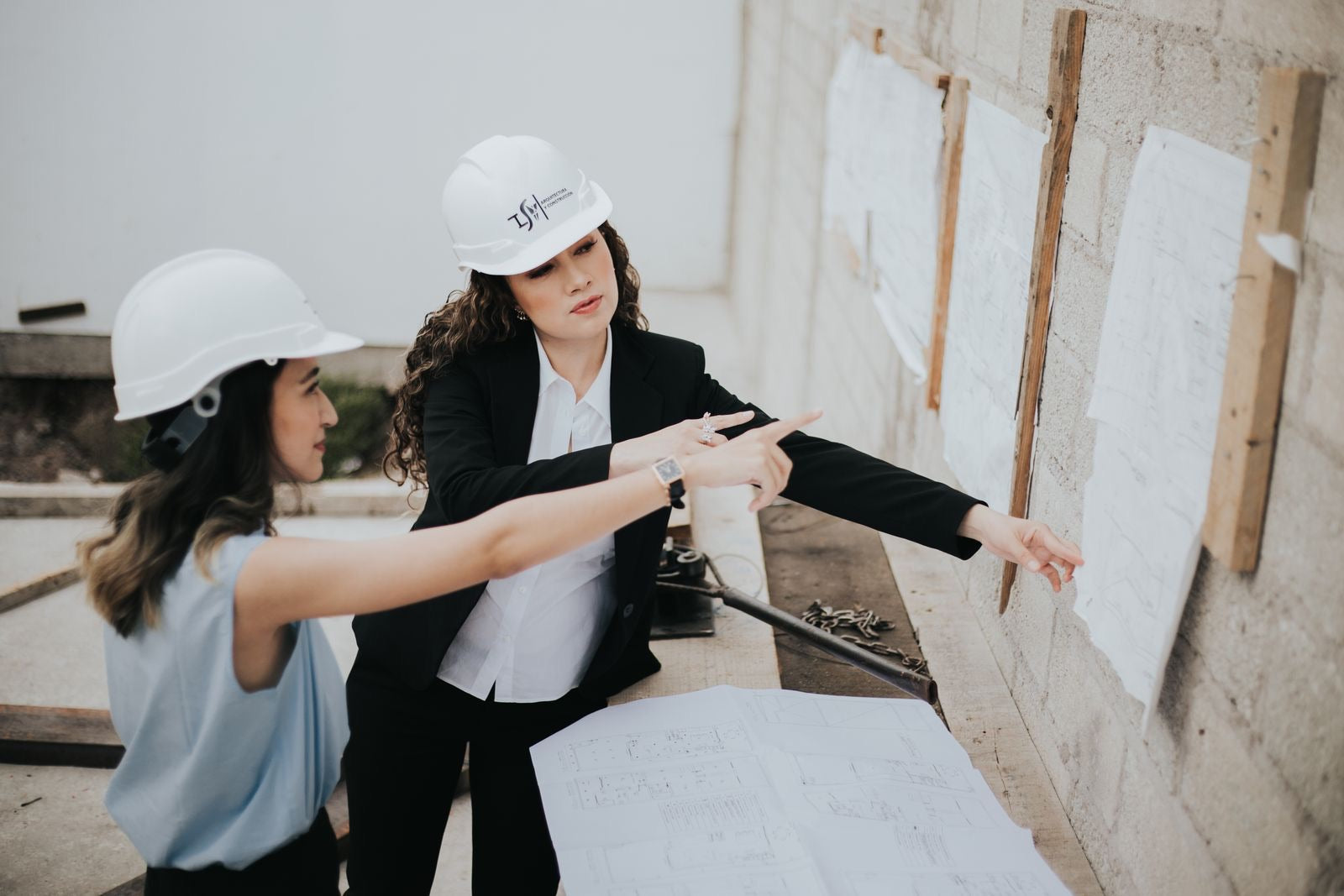 Two architects in hard hats reviewing project drawings on a wall at a construction site, weighing the LEED Green Associate against the LEED AP credential