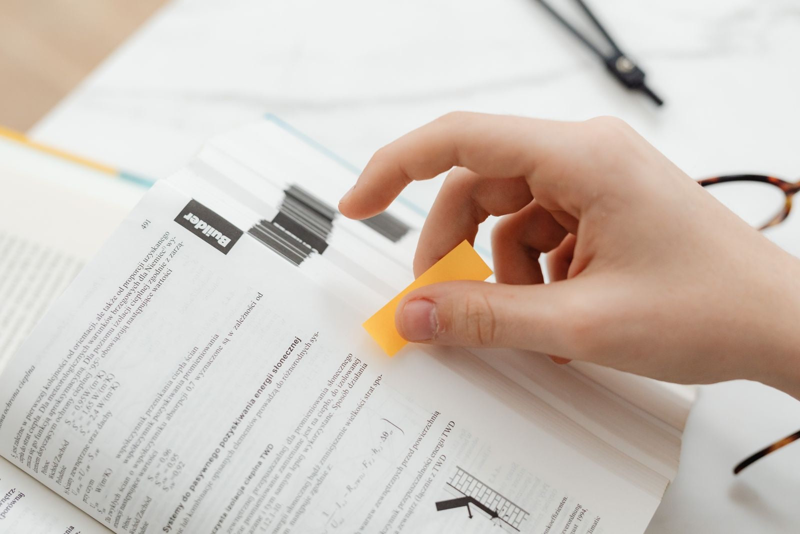 Hand placing a sticky-note tab on a page of a thick technical manual, the way project teams mark credits in the LEED reference guide