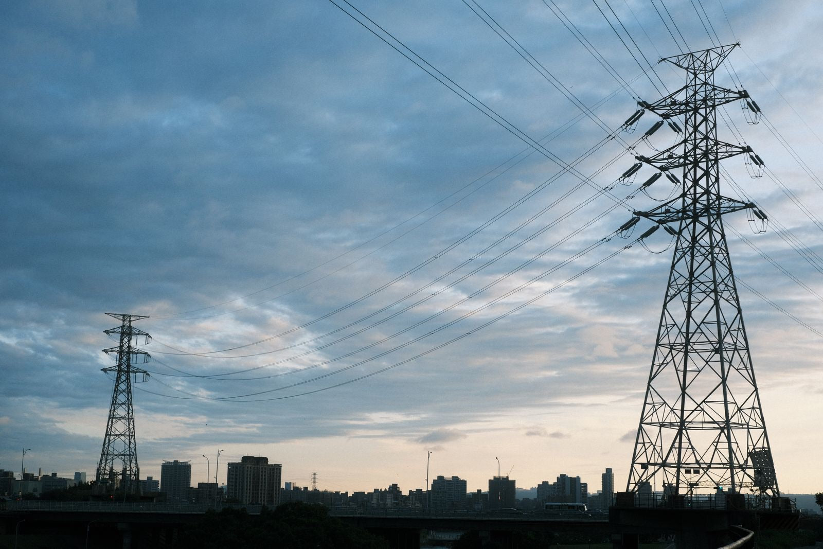 Electric grid transmission lines at dusk with city buildings, the system demand response keeps stable