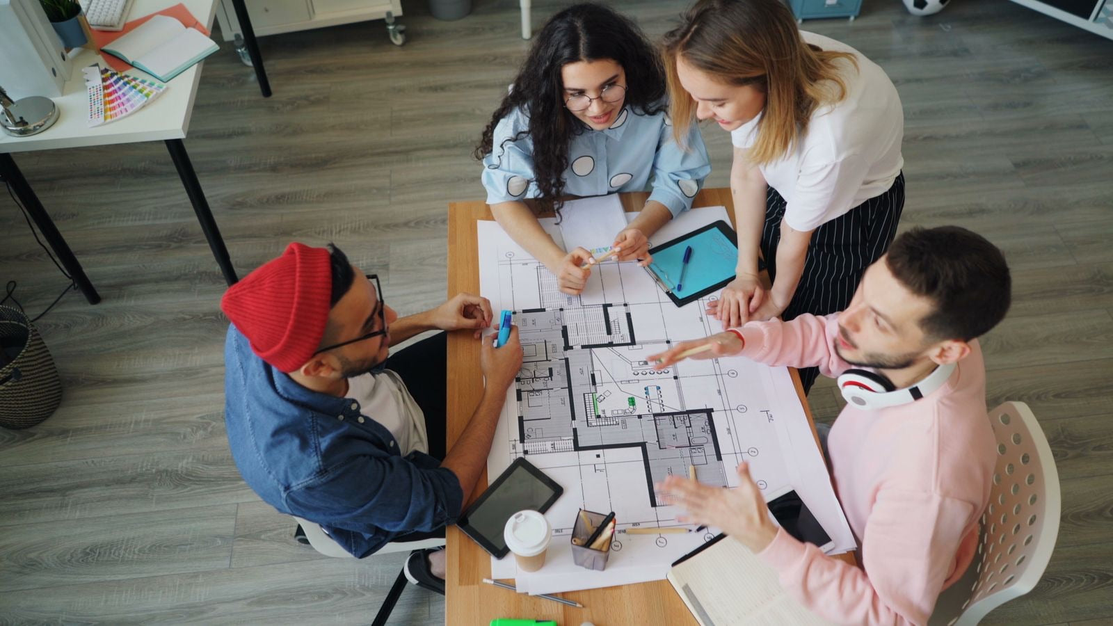 Design team collaborating around one floor plan at a shared table, the whole-team working session at the heart of integrative design